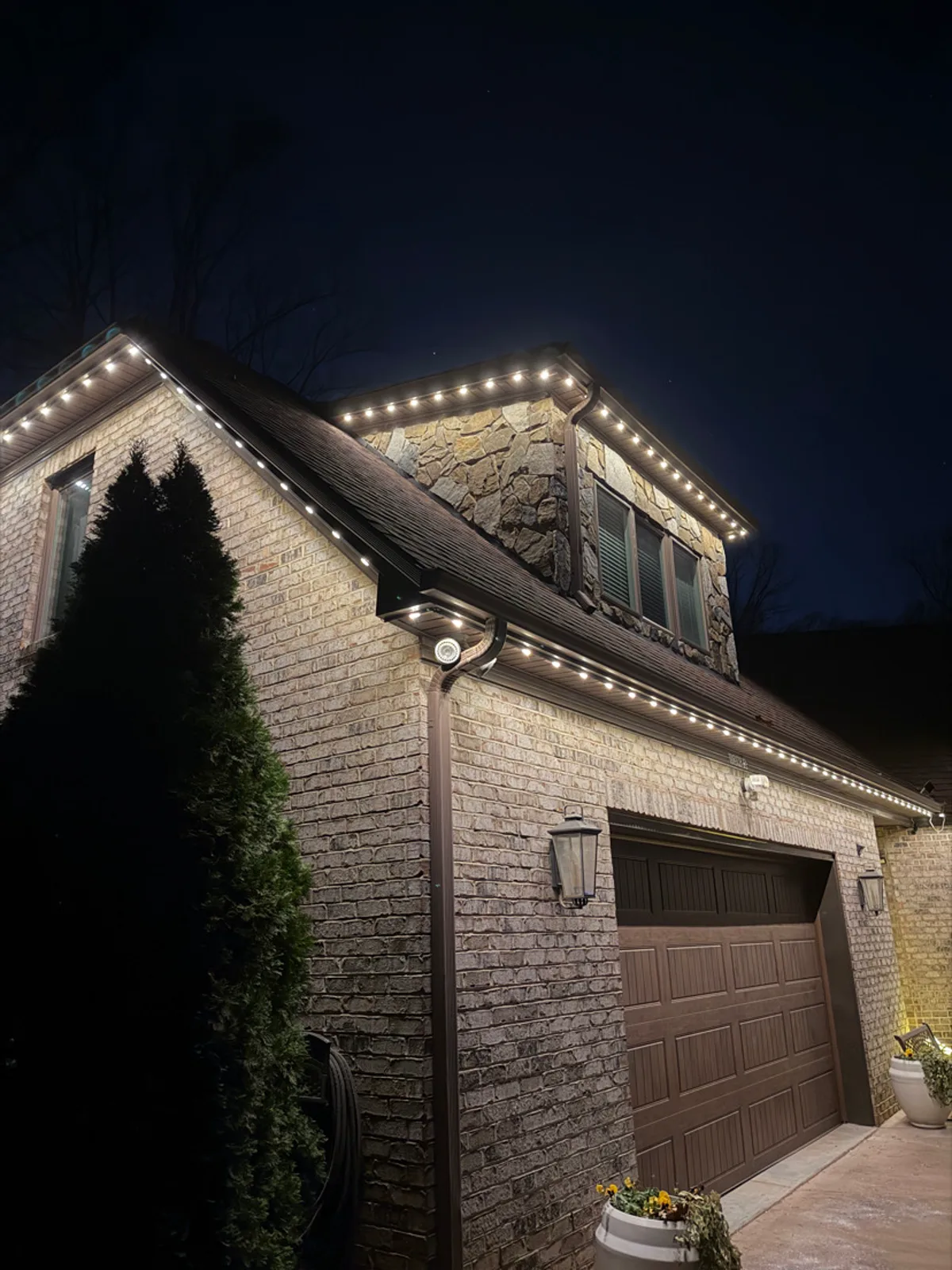 Brick garage and stone dormer with warm-white C9 bulbs along the eaves