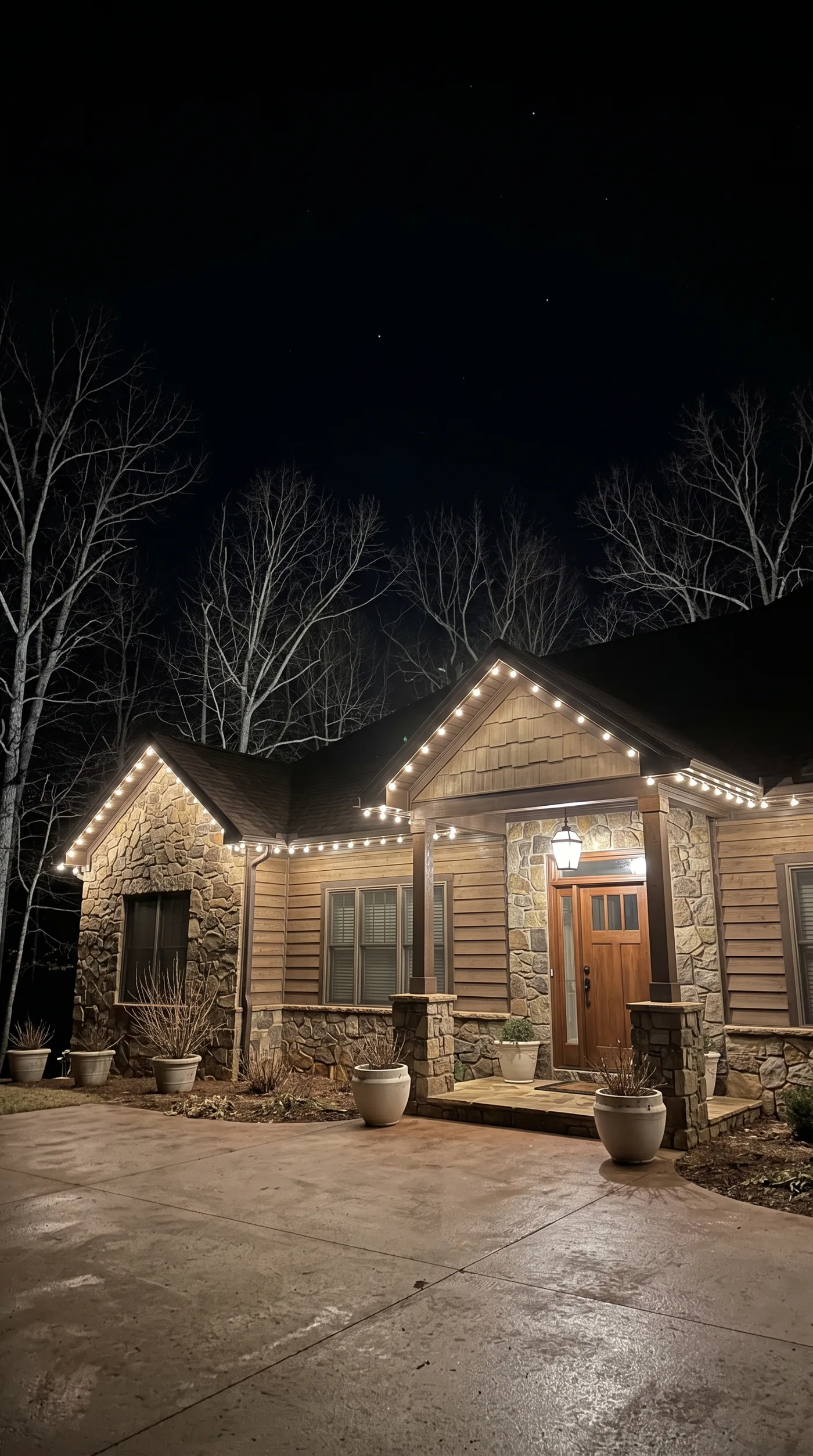Stone and cedar home with warm-white bulbs along the rooflines